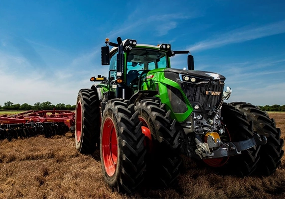 Fendt tractor with dual rear wheels pulling tillage equipment across a dry field under a clear blue sky.