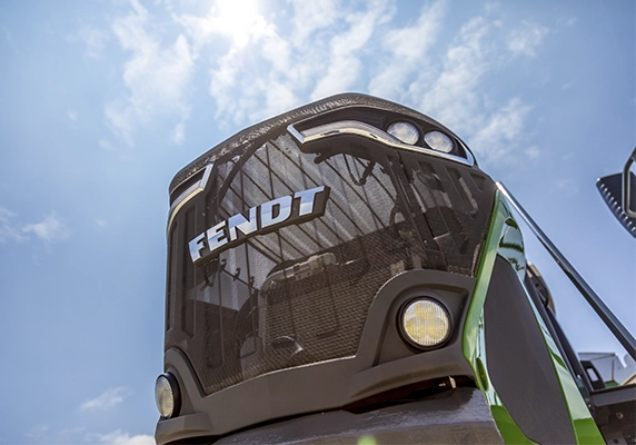 Close-up view of a Fendt tractor grille and headlights under a bright blue sky.