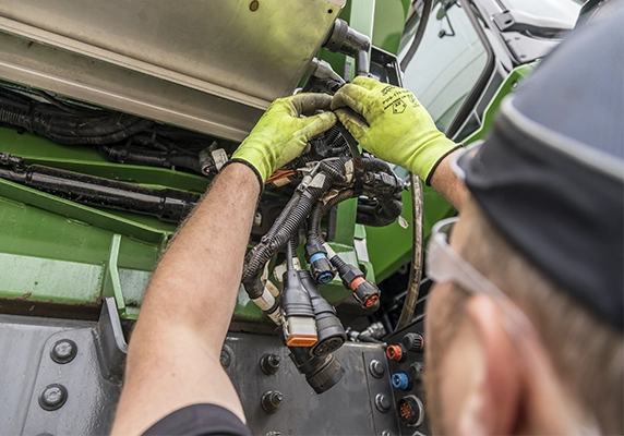 Technician working on the wiring of a SmartAg application lift system on a Fendt tractor.